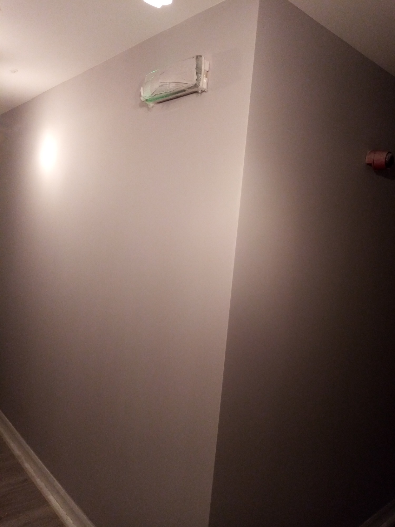 Świeżo pomalowana, szara ściana z zabezpieczonym elementem instalacji elektrycznej folią ochronną i widoczną rolką taśmy malarskiej w rogu.