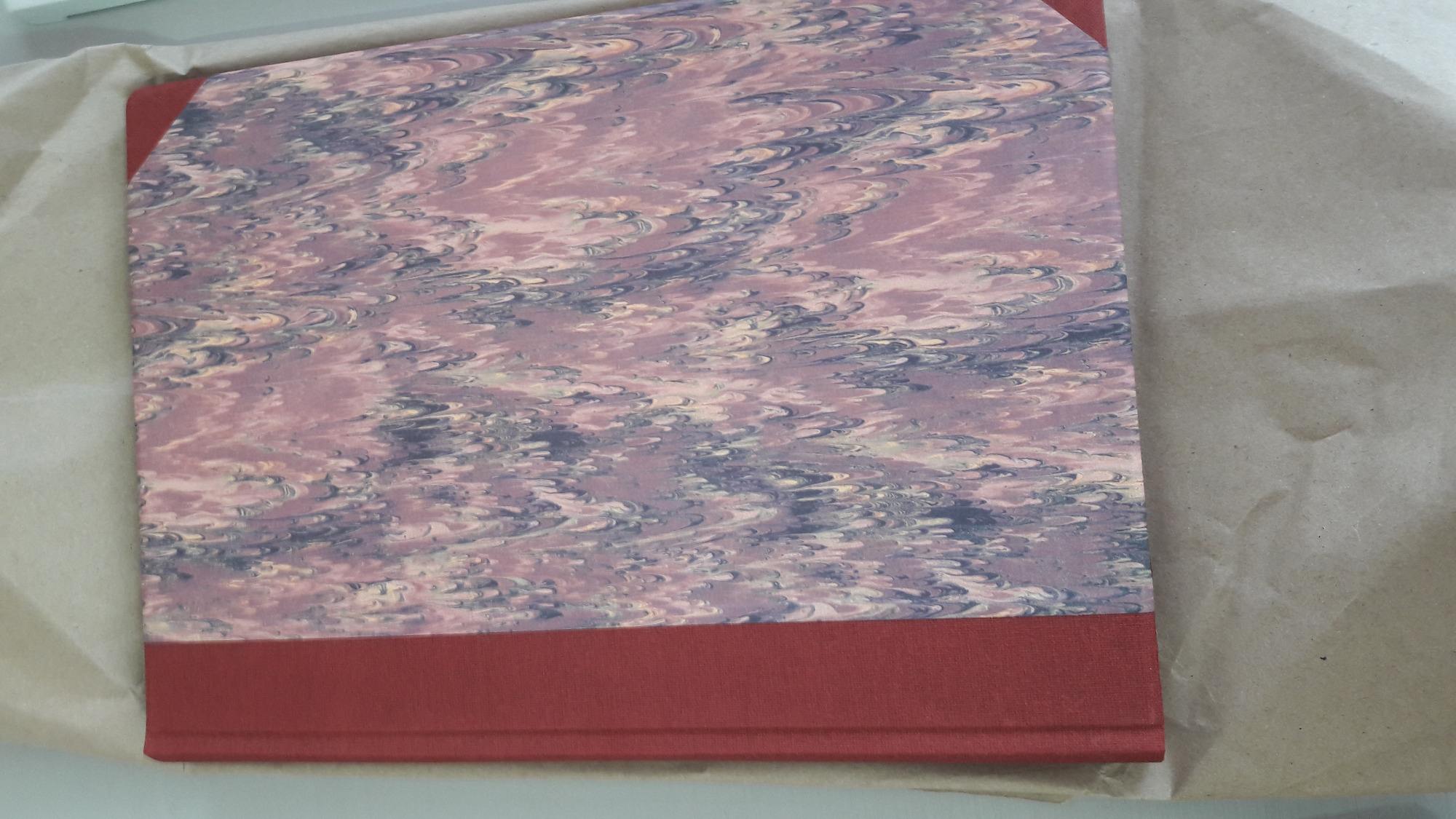 Książka w twardej oprawie z marmurkowym wzorem na okładce, zabezpieczona brązowym papierem pakowym.