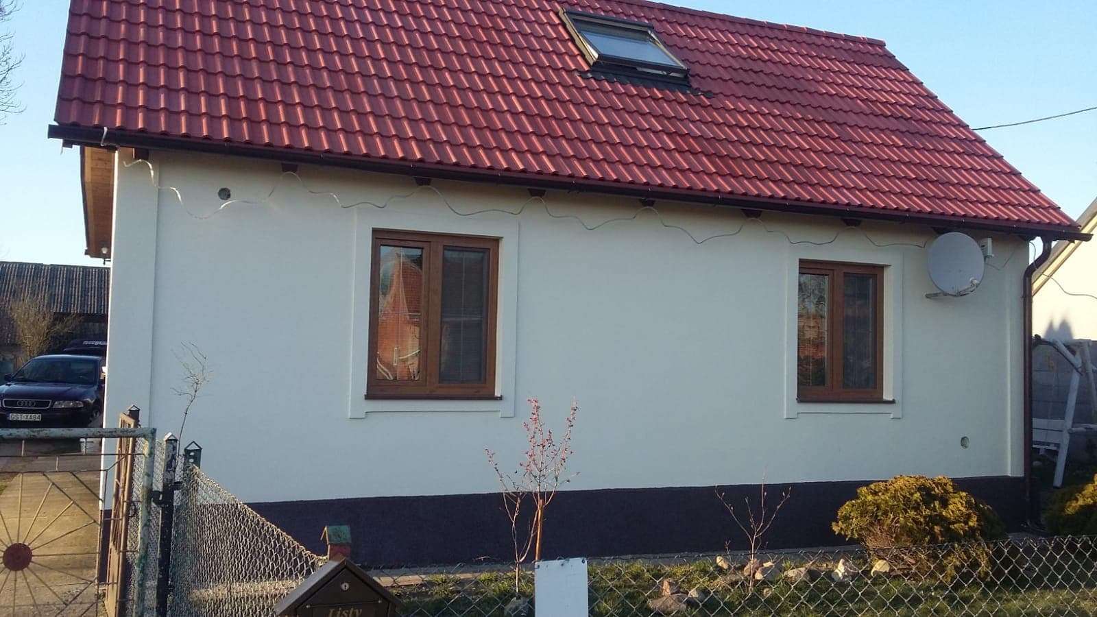 Dom jednorodzinny po tynkowaniu elewacji, z widocznymi brązowymi oknami, czerwoną dachówką i anteną satelitarną na ścianie bocznej.