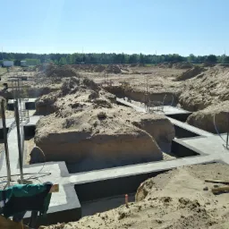 Fundamenty domu jednorodzinnego w Strzegomiu po zalaniu betonem, widoczne zbrojenia i wykopane rowy, teren piaszczysty.