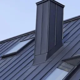 Szary dach z blachy trapezowej z trzema oknami dachowymi i kominem blaszany, widok z dołu.
