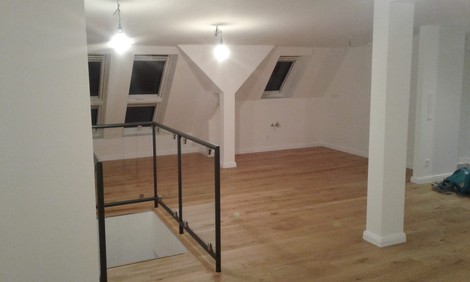 Jasne poddasze z drewnianą podłogą, oknami dachowymi i szklaną balustradą schodów.