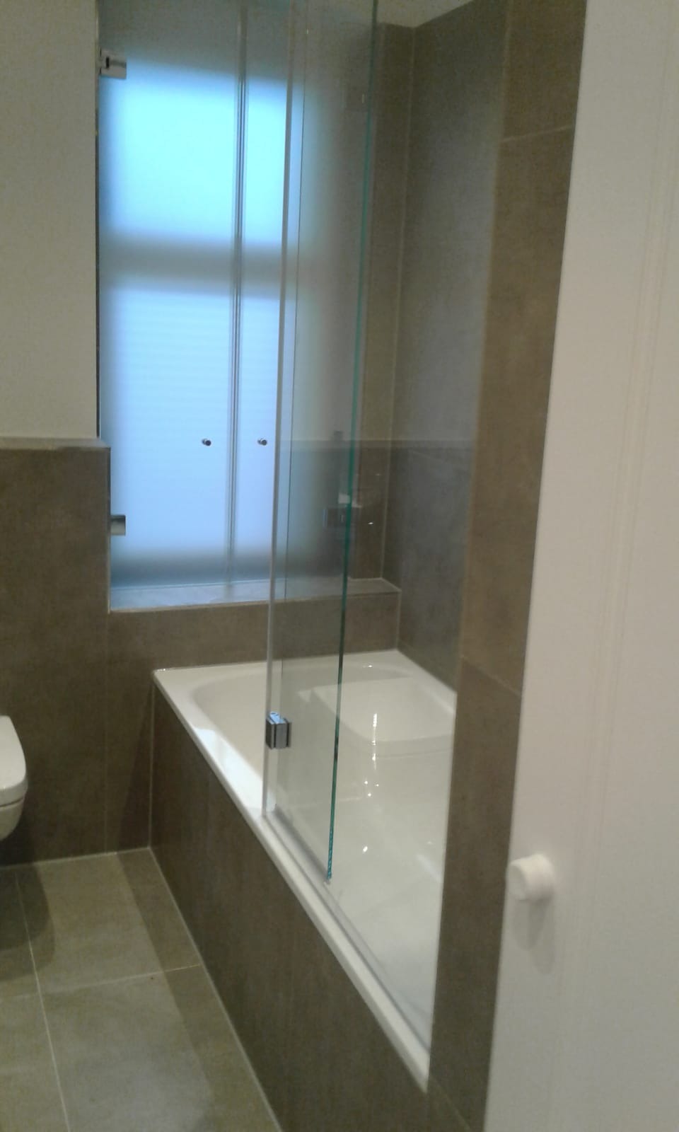 Wykończona łazienka w Przytocznej z nowoczesną kabiną prysznicową z przesuwnymi szklanymi drzwiami, wykończona w odcieniach szarości z widoczną toaletą i fragmentem drzwi.