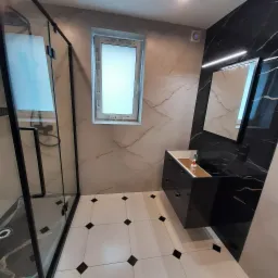 Nowoczesna łazienka z czarną armaturą, kabiną prysznicową typu walk-in, biało-czarną podłogą w karo oraz umywalką z szafką w kolorze czarnym z blatem imitującym marmur.