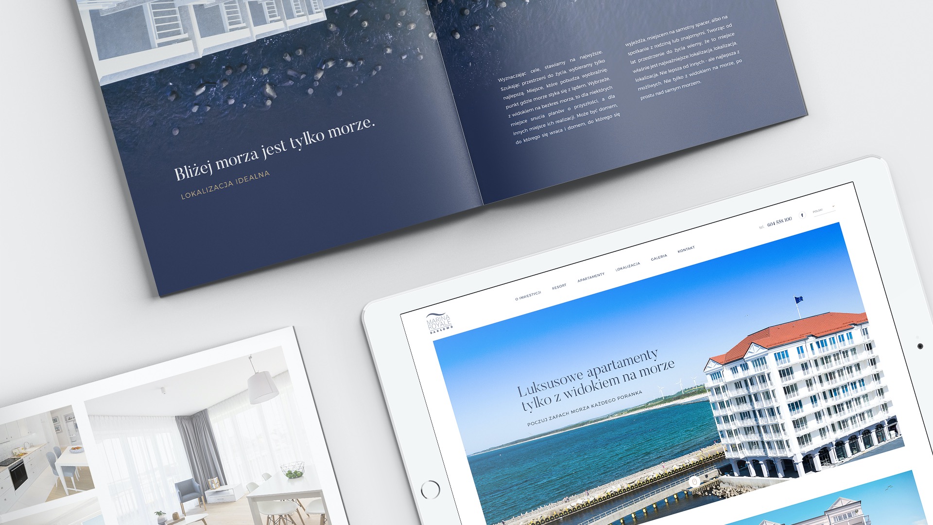 Prezentacja strony internetowej z ofertą luksusowych apartamentów nad morzem na tablecie, obok leży otwarta broszura reklamowa z widokiem na morze i opisem lokalizacji.