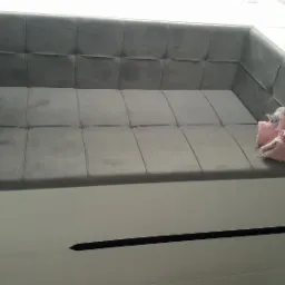 Szara, tapicerowana wnęka z białymi, lakierowanymi bokami, uzupełniona parą różowych, pluszowych kapci z motywem jednorożca.