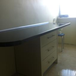 Meble Pod Wymiar - Fragment blatu kuchennego z szufladami w kolorze ecru, widoczny fragment ściany i krzesło w tle, Radomsko.