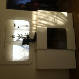 Meble Pod Wymiar - Biała szafa wnękowa z lustrem i dekoracją świąteczną, oświetlona promieniami słonecznymi padającymi przez okno z żaluzjami.