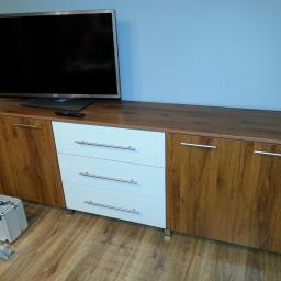 Meble Pod Wymiar - Szafka RTV z drewnopodobnymi frontami i trzema białymi szufladami, na blacie telewizor, obok skrzynka z okuciami do montażu szuflad.