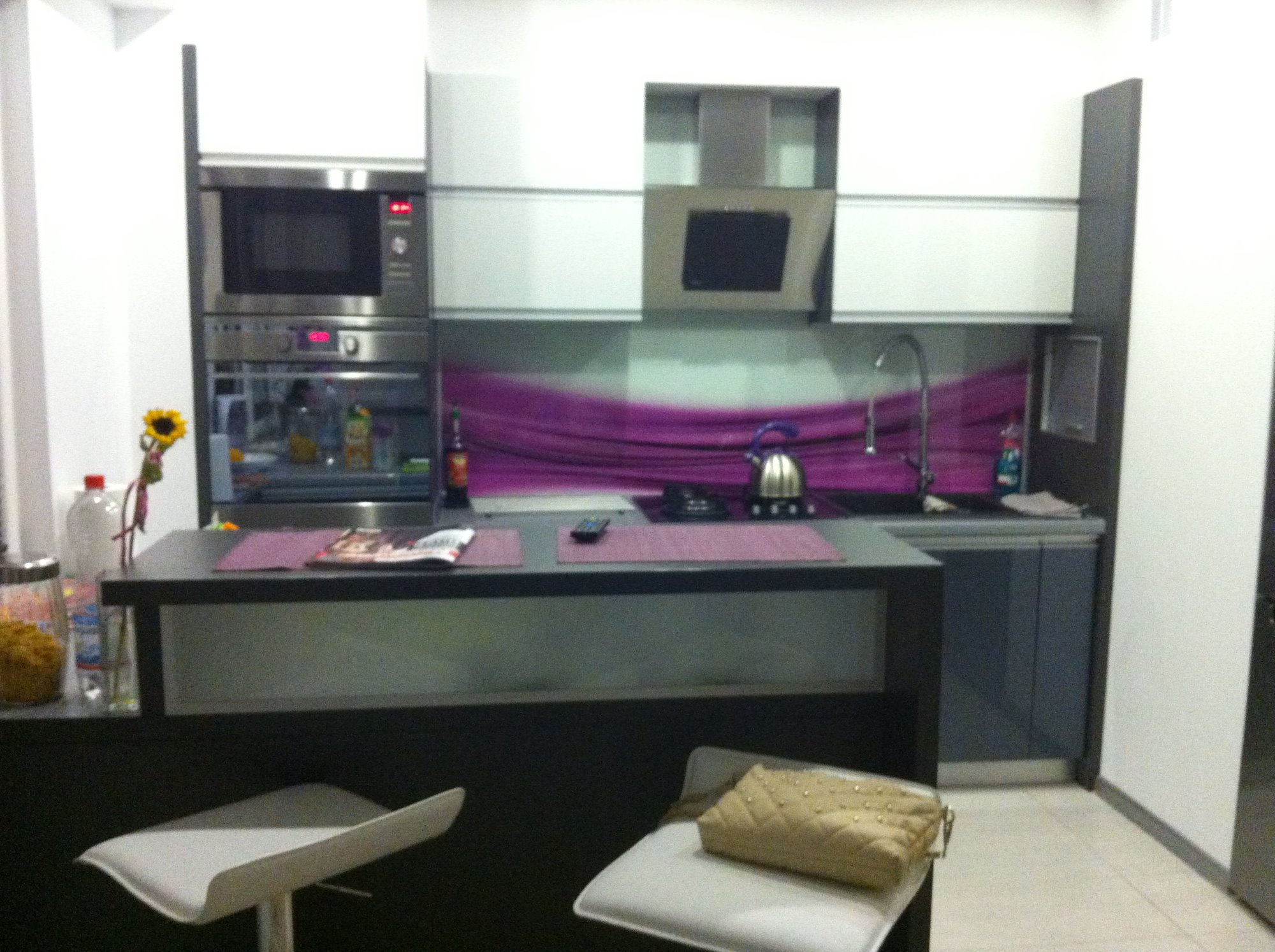 Nowoczesna kuchnia z wyspą, biało-szare szafki, fioletowy panel nad blatem, wysokie krzesła barowe, torebka na jednym z krzeseł, Bełchatów.