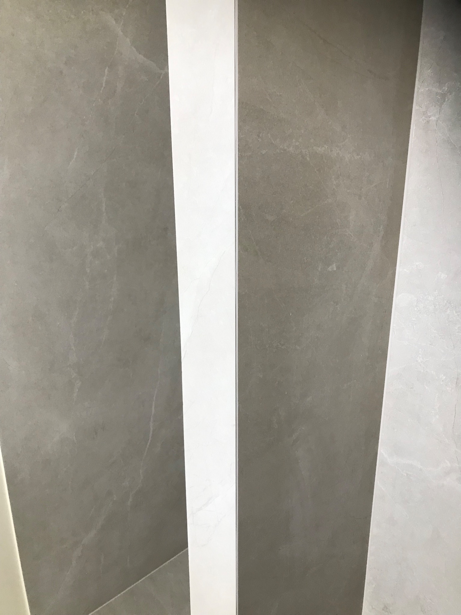 Fragment ściany z szarych i białych, wąskich paneli imitujących marmur, ułożonych pionowo. Widoczne subtelne żyłki i tekstura kamienia.