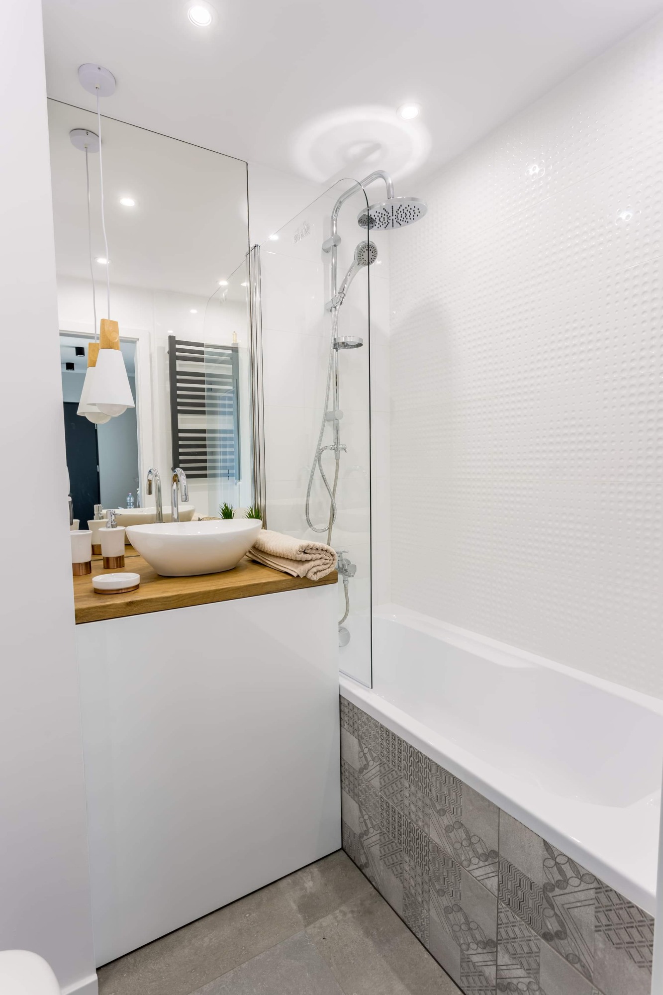 Jasna łazienka z owalną umywalką nablatową na drewnianym blacie, szklanym parawanem nawannowym i mozaiką na obudowie wanny