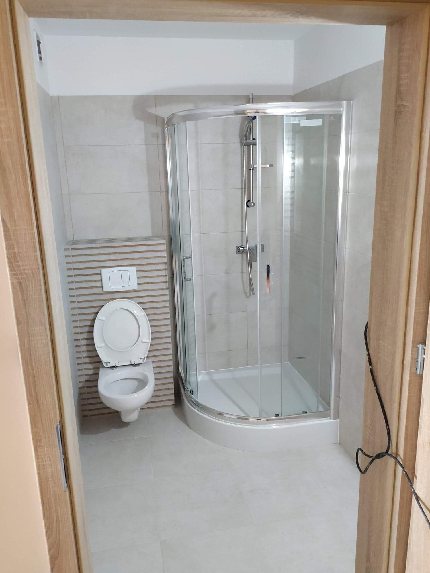 Wyremontowana łazienka w Ełku z narożną kabiną prysznicową, podwieszaną toaletą z zabudową z dekoracyjnych listewek i jasnymi płytkami na ścianach i podłodze.