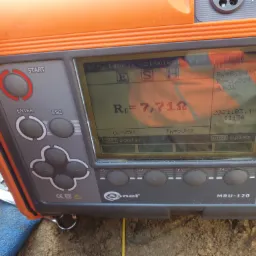 Miernik Sonel MRU-120 wyświetlający wynik pomiaru rezystancji uziemienia 7,71 Ω, z datą 2021.03.19, leżący na ziemi obok narzędzi.