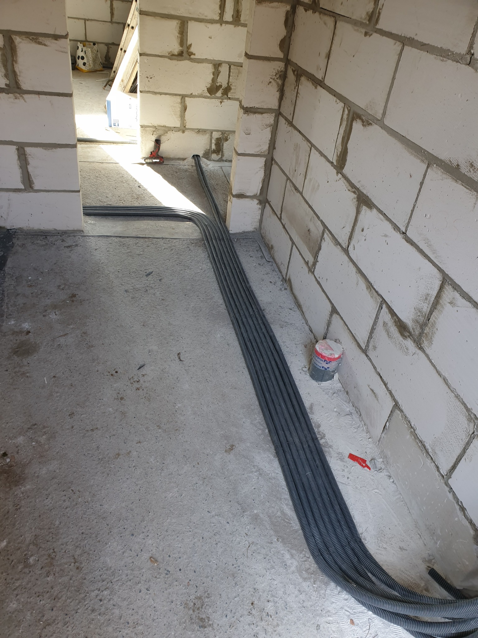 Rury karbowane ułożone wzdłuż ściany z betonu komórkowego w surowym wnętrzu budynku w trakcie budowy, widoczne elementy instalacji elektrycznej.