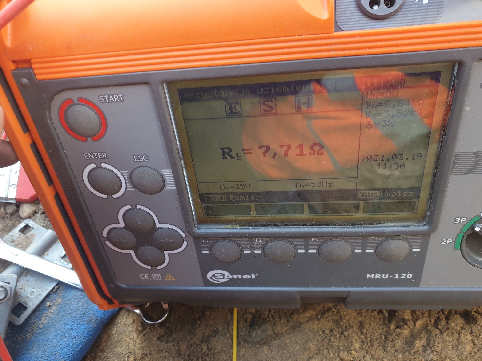 Miernik Sonel MRU-120 wyświetlający wynik pomiaru rezystancji uziemienia 7,71 Ω, z datą 2021.03.19, leżący na ziemi obok narzędzi.
