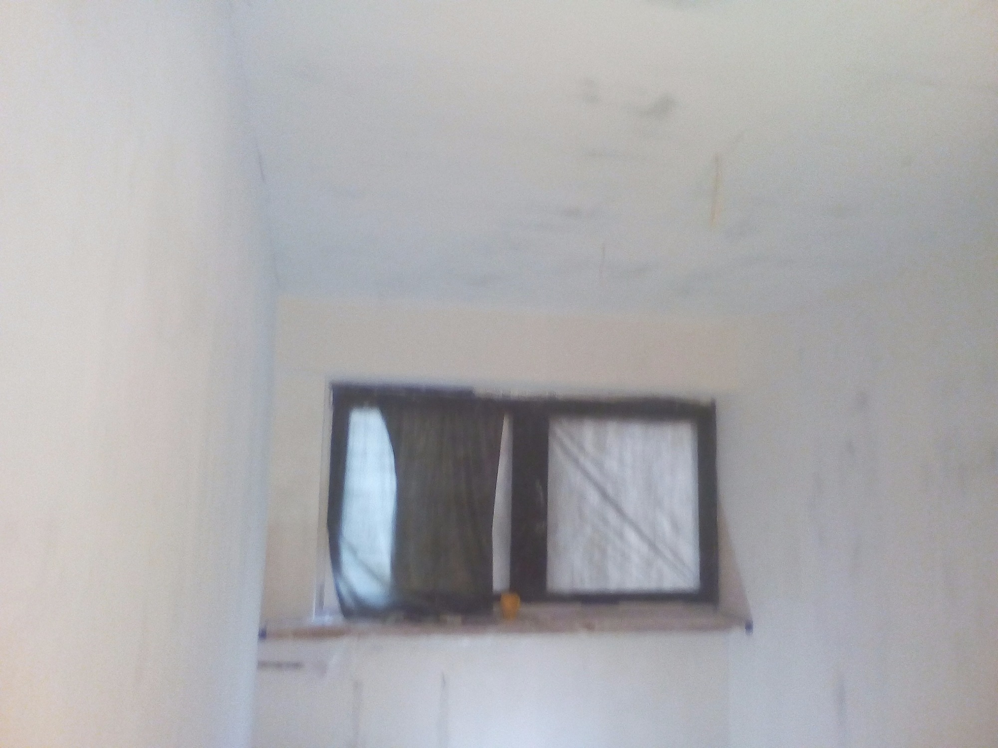 Pokój w trakcie przygotowania do prac wykończeniowych, widoczne zakryte okno i niedoskonałości na ścianach i suficie.