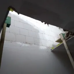 Sufit podwieszany w trakcie montażu, widoczne profile, wełna mineralna i bloczki betonowe w tle.