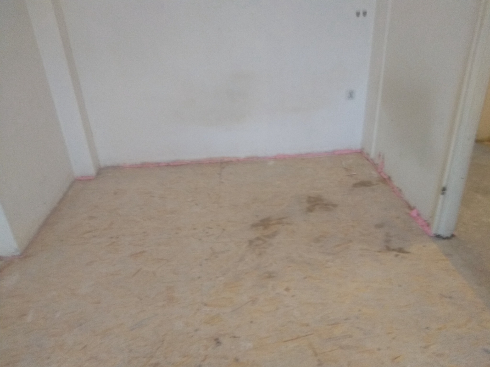 Przygotowanie podłoża pod panele: płyta OSB z widoczną izolacją piankową przy ścianach w pustym pomieszczeniu.