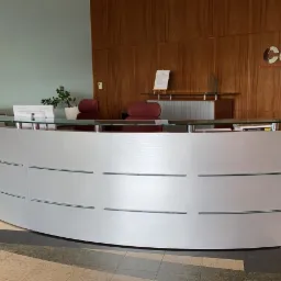 Nowoczesna, zakrzywiona recepcja z białymi panelami i szklanym blatem, przed ścianą z drewnianą okładziną i logo firmy Condix.