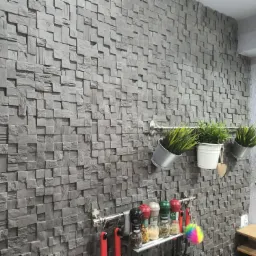 Ściana wykończona szarą, trójwymiarową okładziną z kwadratowych elementów, uzupełniona o wiszące doniczki z roślinami i reling kuchenny z przyprawami.