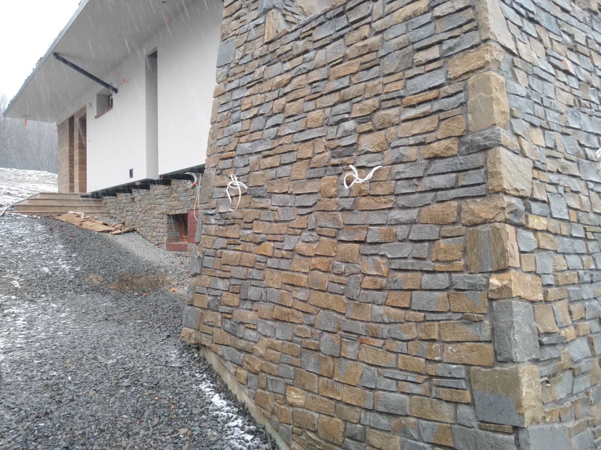 Elewacja budynku wykończona kamieniem w odcieniach szarości i beżu w Brennej, z widocznymi przewodami elektrycznymi i kamiennym podmurówką.