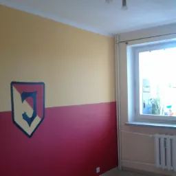 Pokój po malowaniu z poziomym podziałem kolorystycznym ścian: górna część w odcieniu żółci, dolna w kolorze bordo, na ścianie herb w ciemnej obwódce, widoczne grzejniki i okno.
