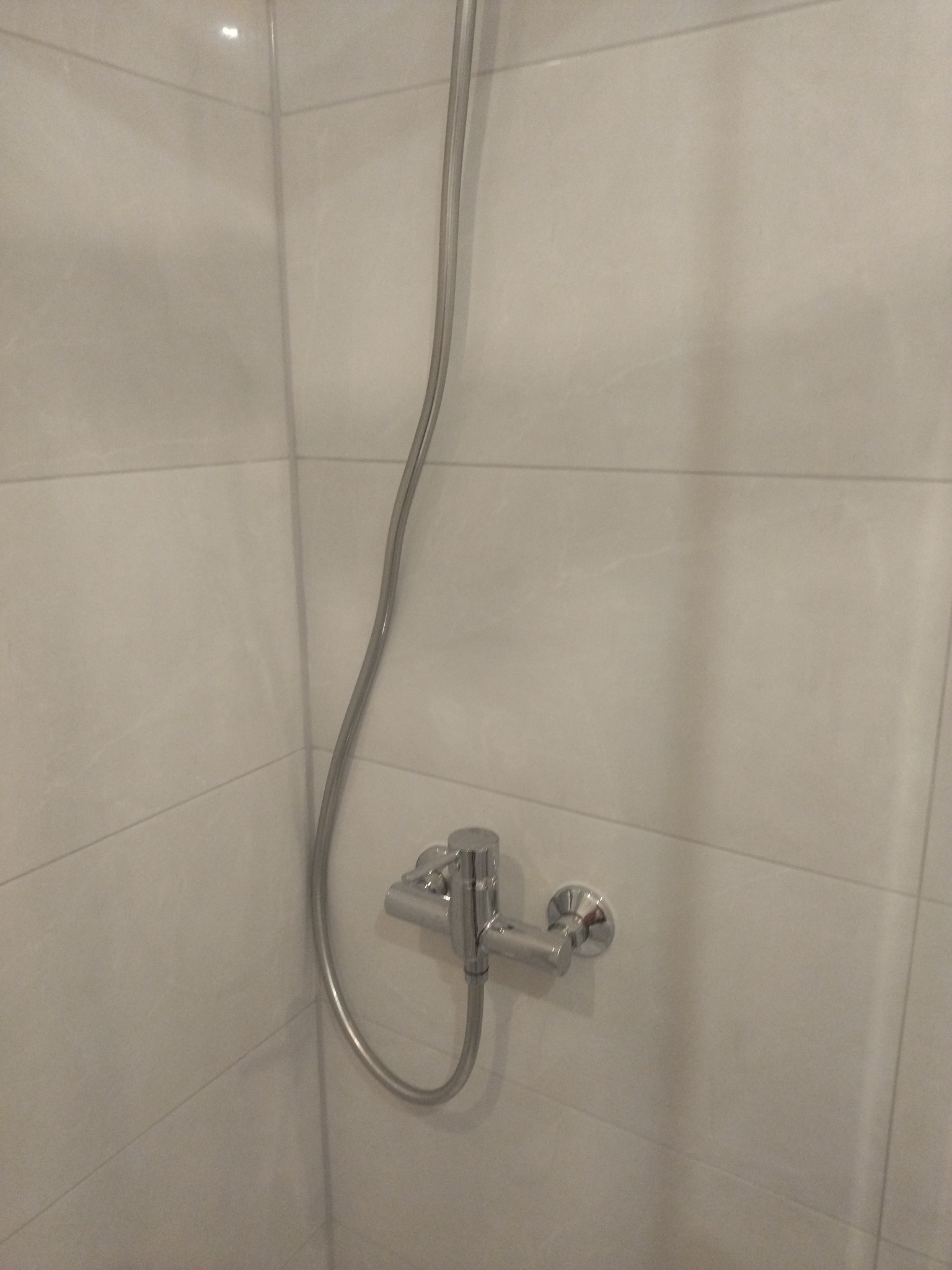 Bateria prysznicowa z chromowanym wykończeniem na tle białych, prostokątnych płytek w kabinie prysznicowej.