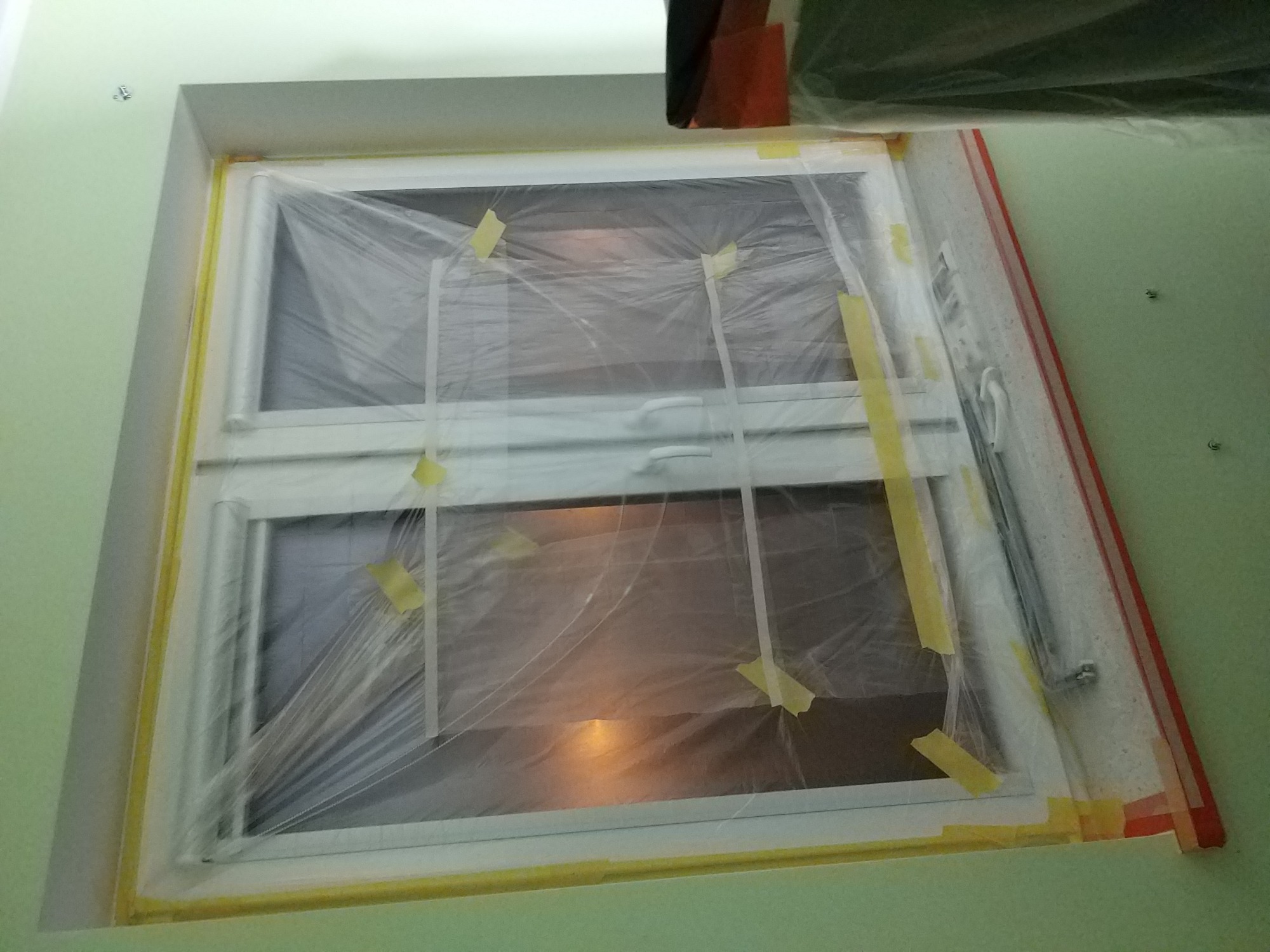 Okno zabezpieczone folią i taśmą malarską przed malowaniem ścian w odcieniach zieleni.