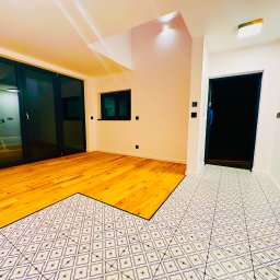 Usługi Remontowo Wykończeniowe PIOTR LEONOWICZ - Jasne wnętrze z parkietem i wzorzystą podłogą w korytarzu. Widoczne duże okna balkonowe i drzwi. Kontrast materiałów i kolorów. Nowoczesne wykończenie.