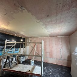 Usługi Remontowo Wykończeniowe PIOTR LEONOWICZ - Pokój w trakcie prac wykończeniowych: częściowo wygładzony sufit, rusztowanie, zabezpieczone okno folią. Widoczne ślady po instalacjach elektrycznych na ścianach.