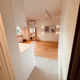 Usługi Remontowo Wykończeniowe PIOTR LEONOWICZ - Jasne wnętrze po remoncie: parkiet, białe ściany, oświetlenie punktowe, dekoracyjne obrazy. Widok z korytarza na odnowiony pokój z elementami wyposażenia.