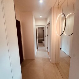 Usługi Remontowo Wykończeniowe PIOTR LEONOWICZ - Nowoczesny korytarz z beżową podłogą, białymi ścianami i szafami w zabudowie. Okrągłe, wiszące lampy z ledowym oświetleniem. W tle widoczna łazienka.