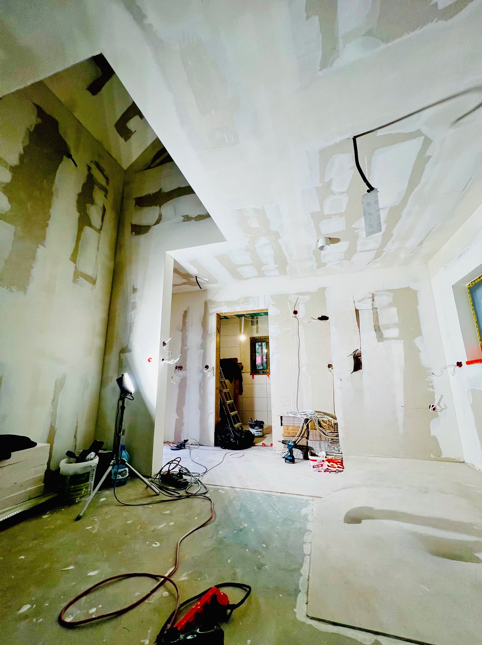 Wnętrze w trakcie prac wykończeniowych w Warszawie. Widoczne ściany z płyt karton-gips, instalacje elektryczne i narzędzia. Oświetlenie robocze.