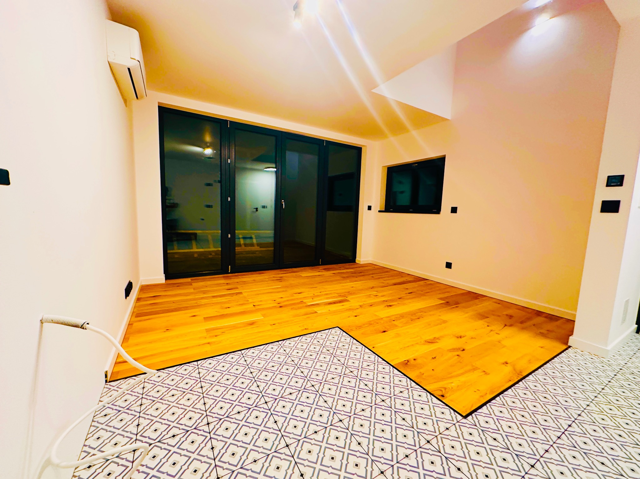 Jasne panele podłogowe przechodzą w dekoracyjne płytki w przestronnym, odnowionym wnętrzu z dużymi, przeszklonymi drzwiami balkonowymi i klimatyzacją.