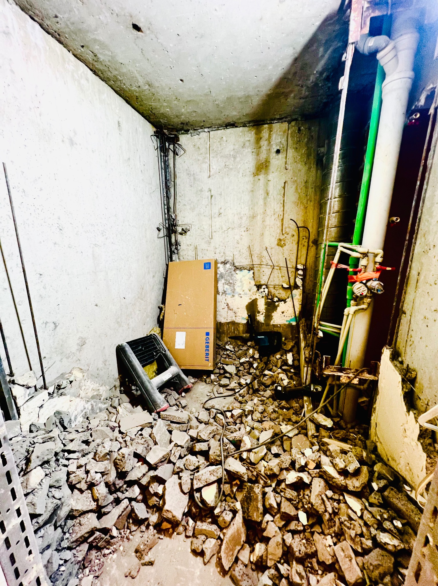 Wnętrze w trakcie demontażu: gruz na podłodze, odsłonięte rury i instalacje, karton Geberit. Przygotowanie do remontu w surowym stanie.