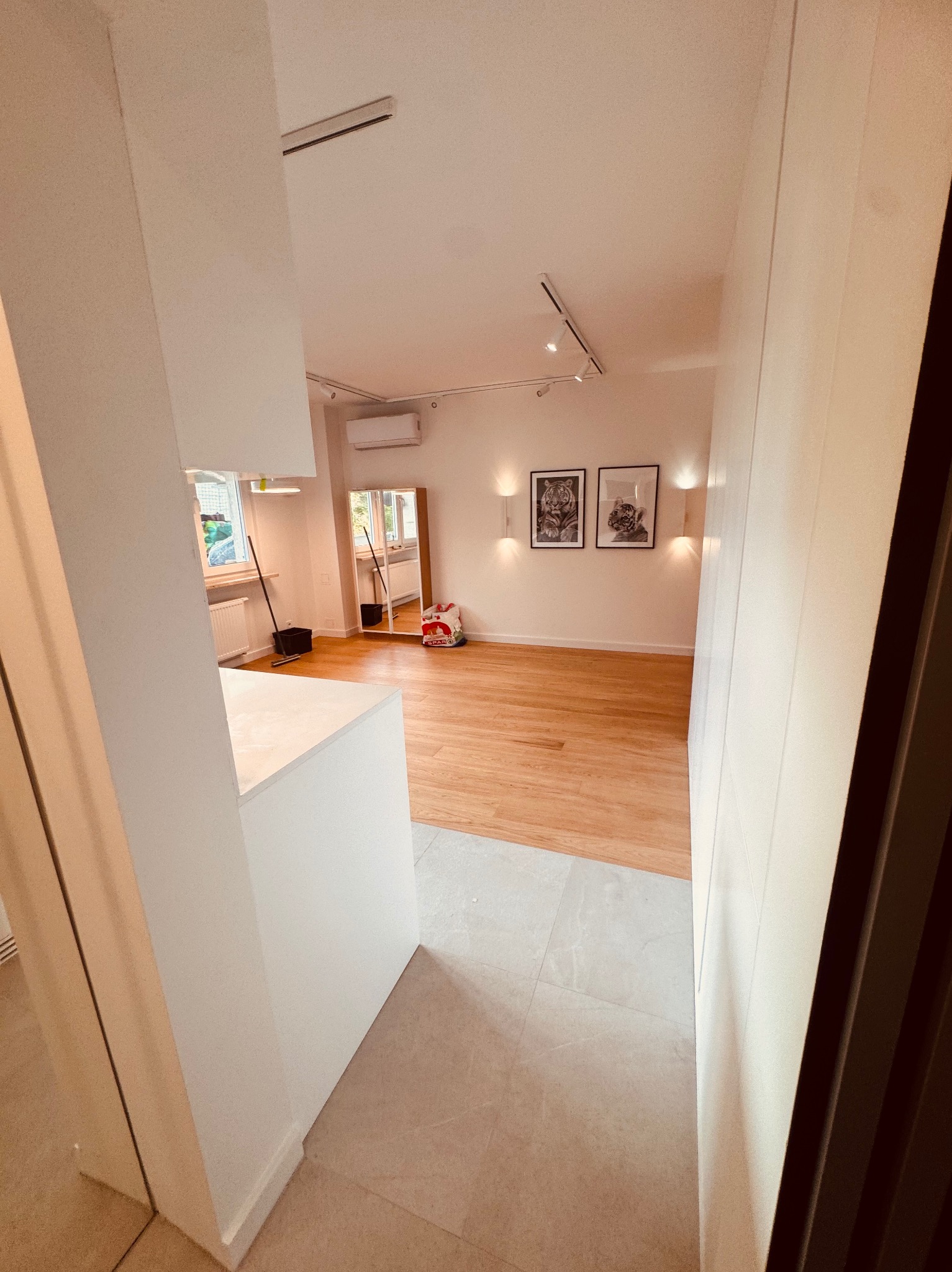 Jasne wnętrze po remoncie: parkiet, białe ściany, oświetlenie punktowe, dekoracyjne obrazy. Widok z korytarza na odnowiony pokój z elementami wyposażenia.