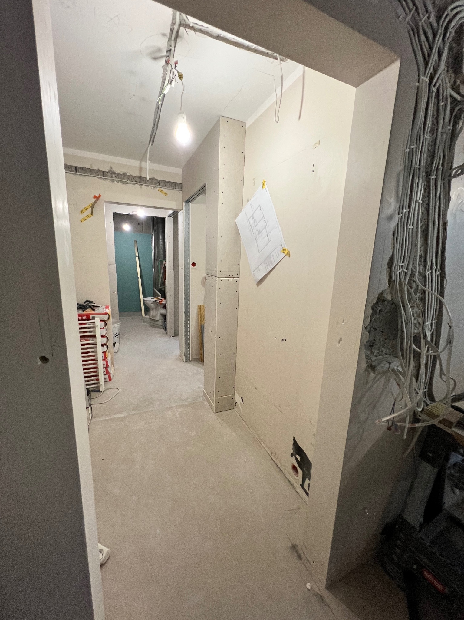 Wnętrze w trakcie remontu: widoczne przewody elektryczne, płyty karton-gips, gładzie na ścianach, plan na ścianie. W tle toaleta w trakcie prac wykończeniowych.