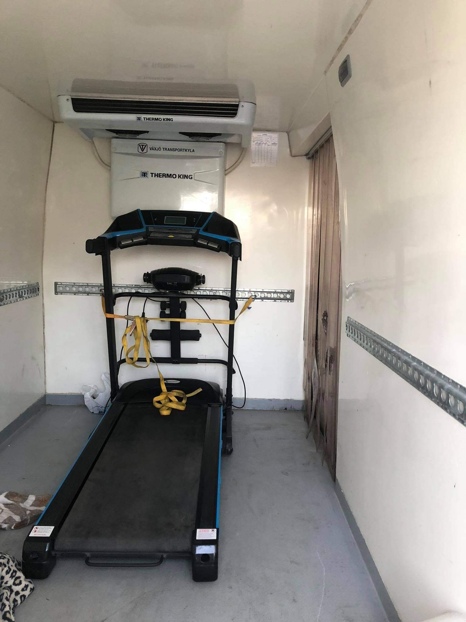 Bieżnia zabezpieczona żółtymi pasami w chłodni transportowej, widoczne szyny mocujące na ścianach i agregat chłodniczy Thermo King.