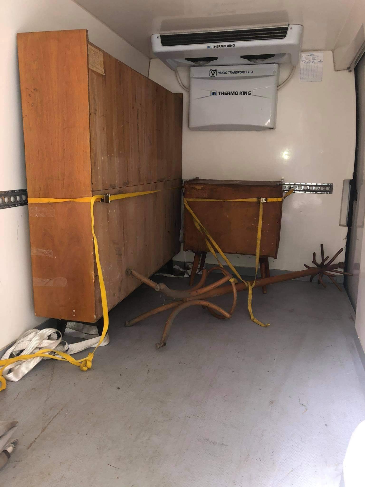 Wnętrze chłodni transportowej z zabezpieczonymi pasami meblami: drewniana szafa i stolik na nóżkach.