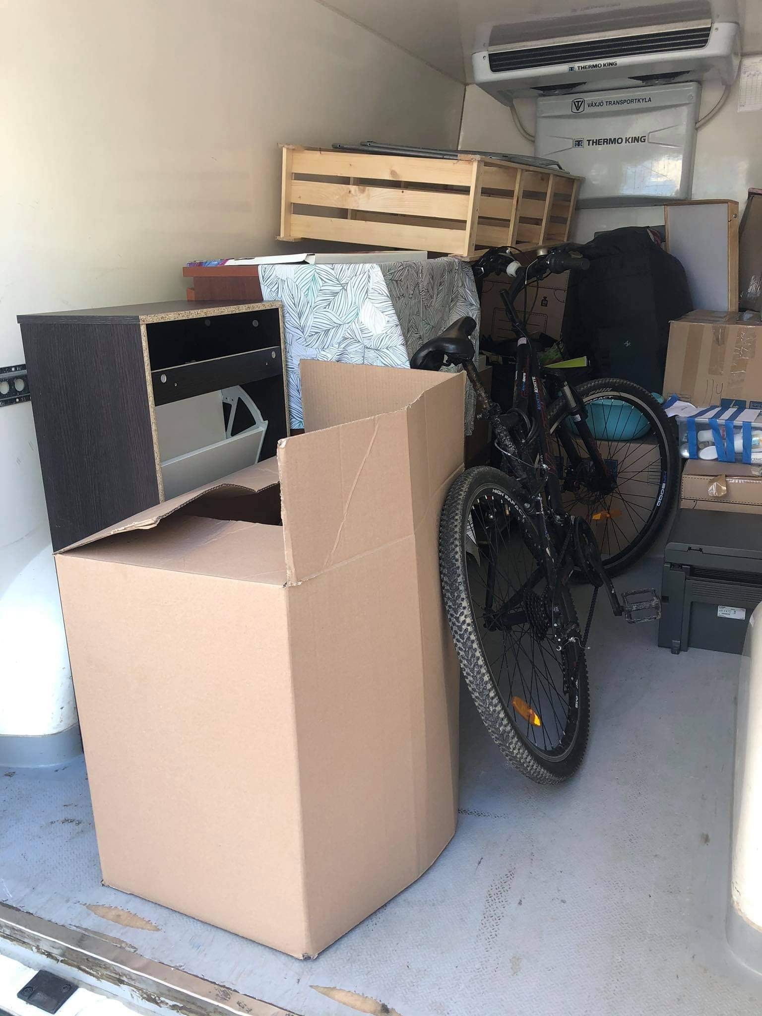 Wnętrze furgonetki załadowane meblami, kartonami i rowerem podczas przeprowadzki, z widoczną jednostką chłodniczą Thermo King na suficie.