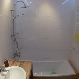 Nowoczesna łazienka z białymi, prostokątnymi płytkami, chromowaną armaturą, drewnianym blatem pod umywalką i grzejnikiem drabinkowym z żółtym ręcznikiem.