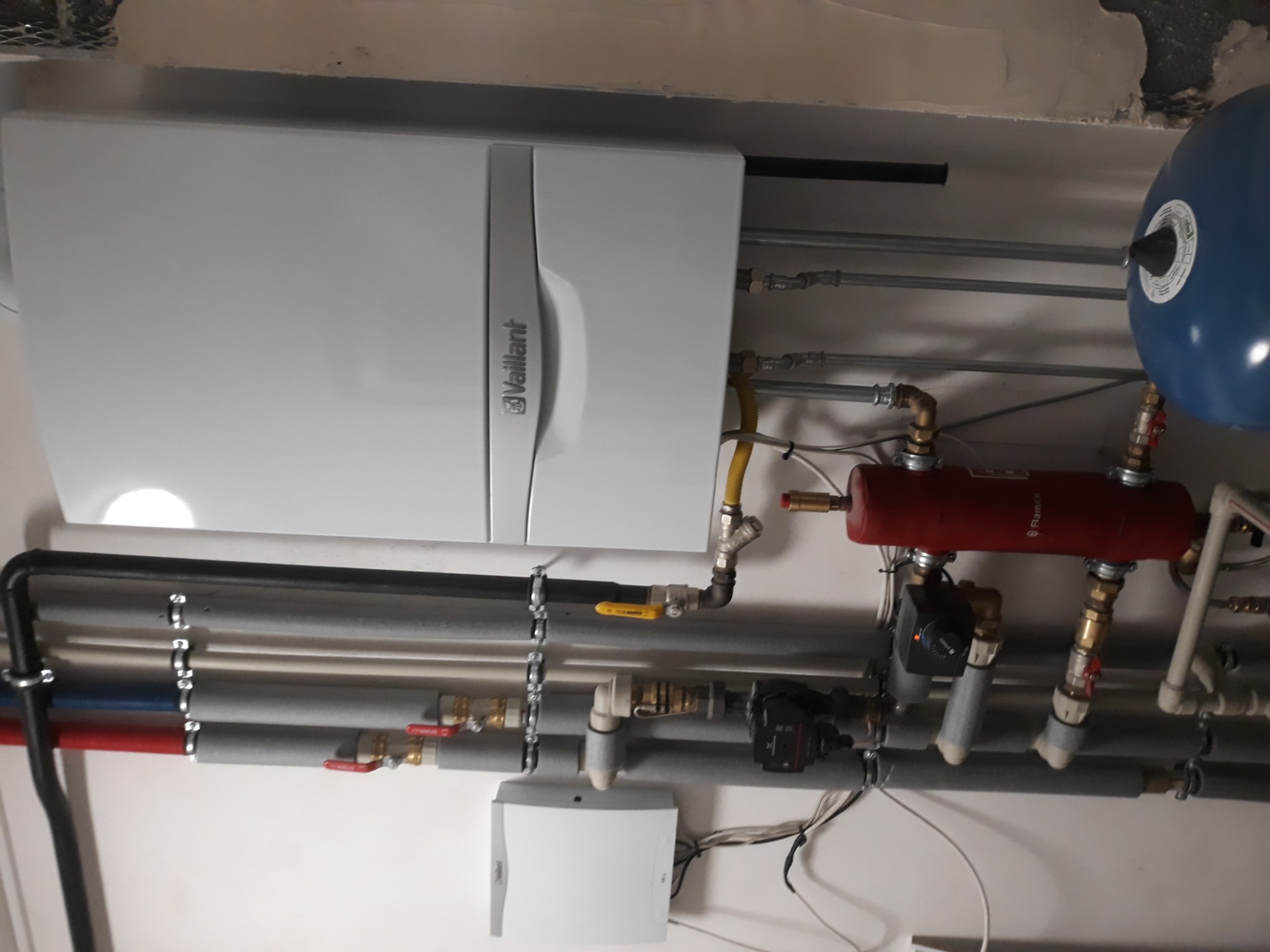 Montaż kotła grzewczego marki Vaillant wraz z osprzętem i orurowaniem w Grodzisku Mazowieckim. Widoczne liczne rury, zawory, zbiornik wyrównawczy oraz regulator temperatury.