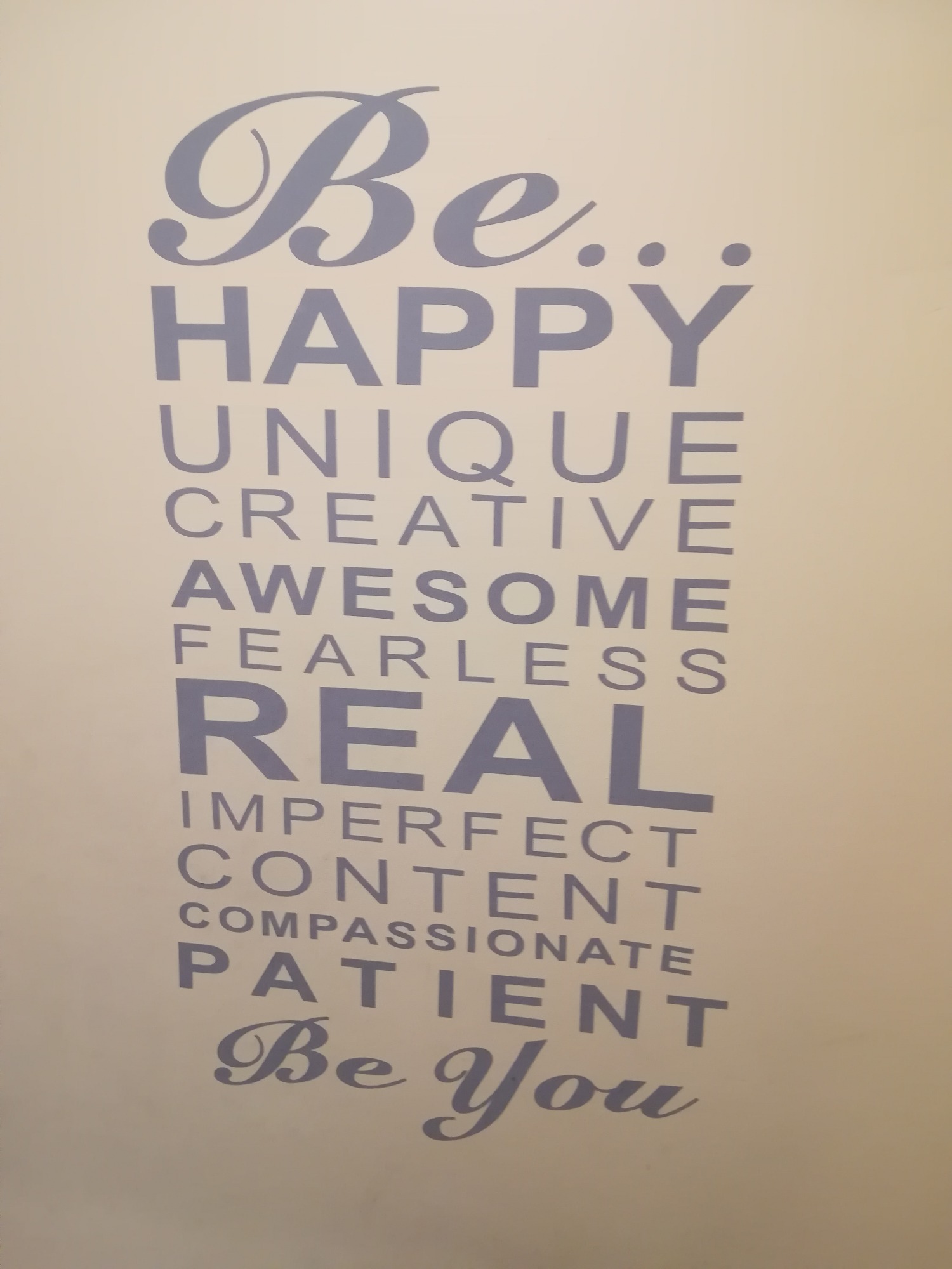Napis na ścianie w kolorze szarym: Be Happy, Unique, Creative, Awesome, Fearless, Real, Imperfect, Content, Compassionate, Patient, Be You