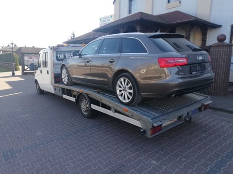 Brązowe Audi A6 Avant na platformie lawety, widok z tyłu, na tle budynku z brązowym dachem.