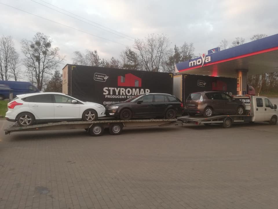 Laweta z trzema samochodami osobowymi (biały Ford Focus, ciemny sedan i brązowy minivan) na przyczepach, stojąca na stacji benzynowej Moya z widocznym billboardem Styromap w tle.