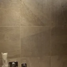 Nowoczesna kabina prysznicowa z deszczownicą i baterią podtynkową, wykończona płytkami imitującymi marmur, z widocznymi śladami użytkowania.