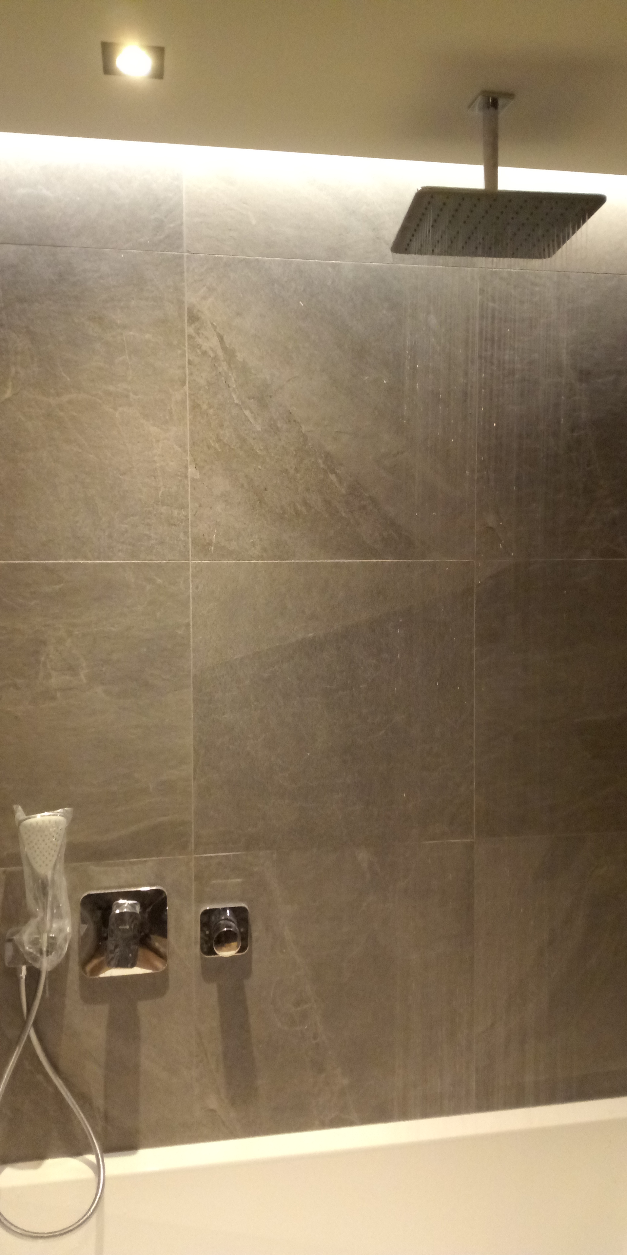 Nowoczesna kabina prysznicowa z deszczownicą i baterią podtynkową, wykończona płytkami imitującymi marmur, z widocznymi śladami użytkowania.