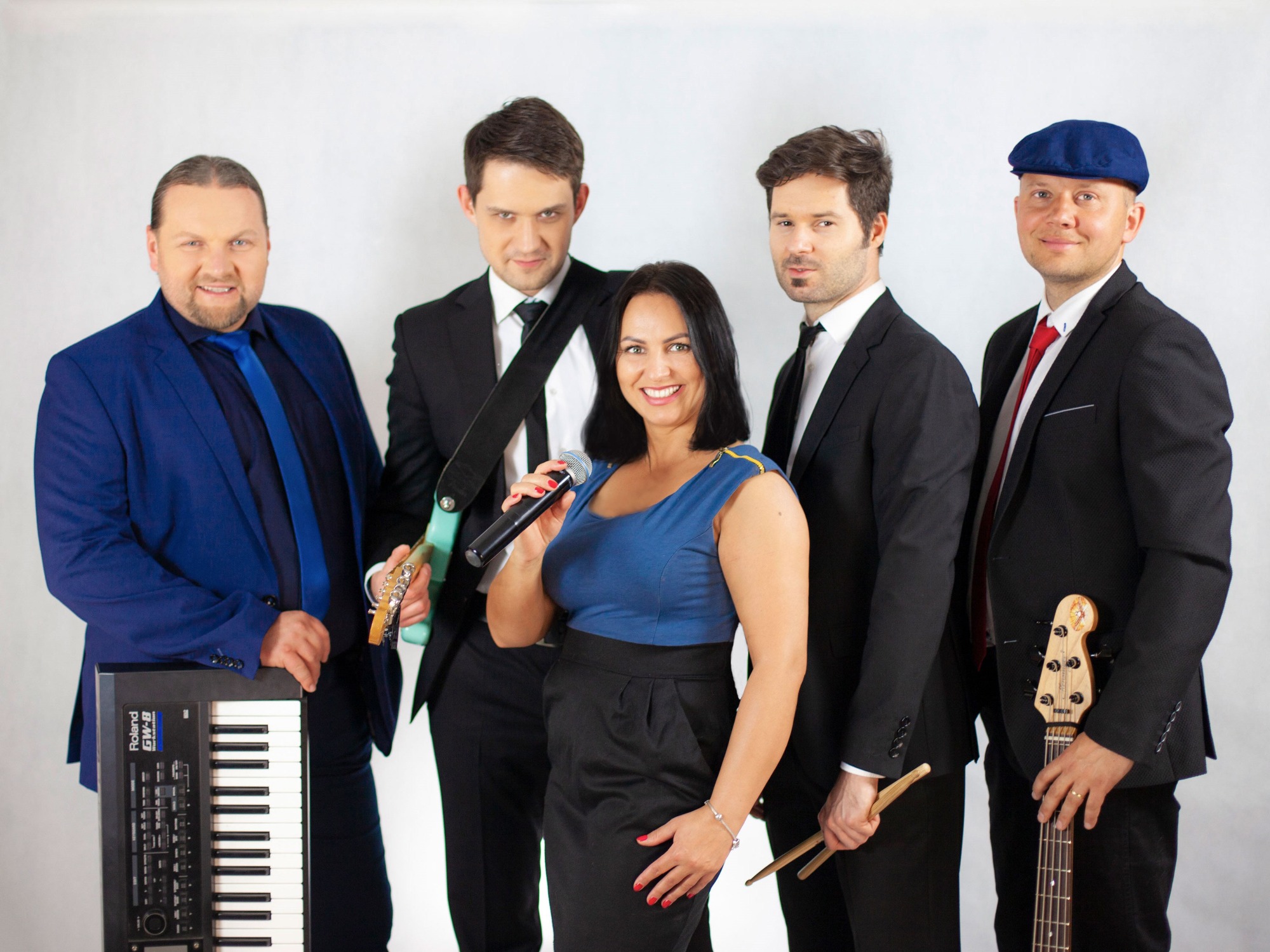 Pięcioosobowy zespół muzyczny w strojach wizytowych pozuje na białym tle, wokalistka z mikrofonem na pierwszym planie, klawiszowiec z Roland GW-8 po lewej, gitarzyści po bokach, perkusista...