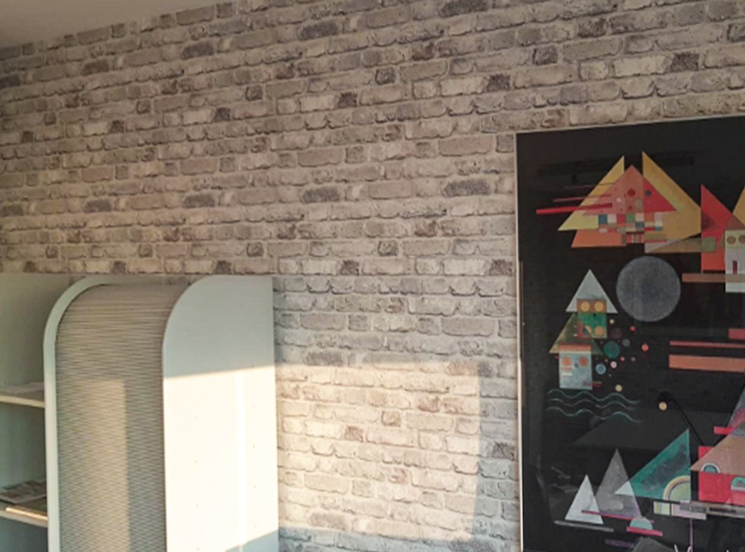 Tapeta imitująca mur z jasnej cegły w pokoju w Poznaniu, obok biały regał i abstrakcyjny obraz na ścianie.